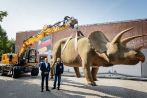 Der Direktor des LWL Dr. Georg Lunemann und Museumsdirektor Dr. Jan Ole Kriegs (von links) markieren den Startschuss am neuen Museumseingang mit dem Triceratops im Hintergrund.(Foto: LWL/Steinweg)